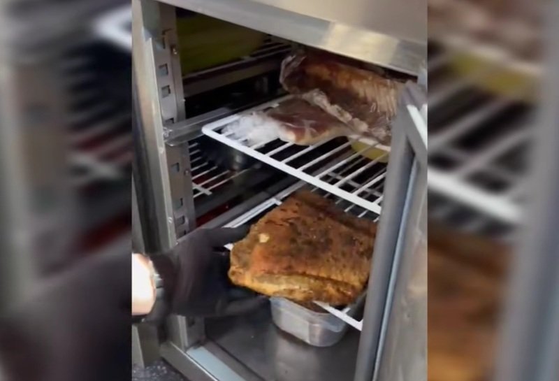 Person in a black glove lifts a large browned roast from a metal smoker/oven rack.