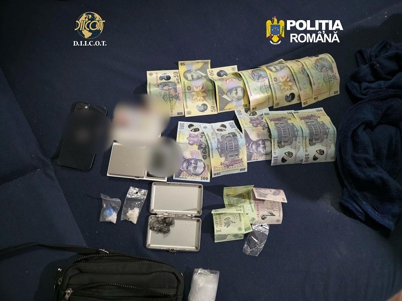 Bundles of money, small bags, and a scale displayed on a dark mat, with DIICOT and Romanian police logos visible