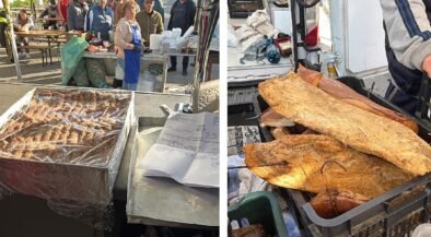 Outdoor market scene: a food stall with grilled skewers on a metal tray and customers lining up behind the counter; tents and people in the background (left). On the right, crates hold large fried flatbreads or pastries ready for sale, near a vendor's gear.