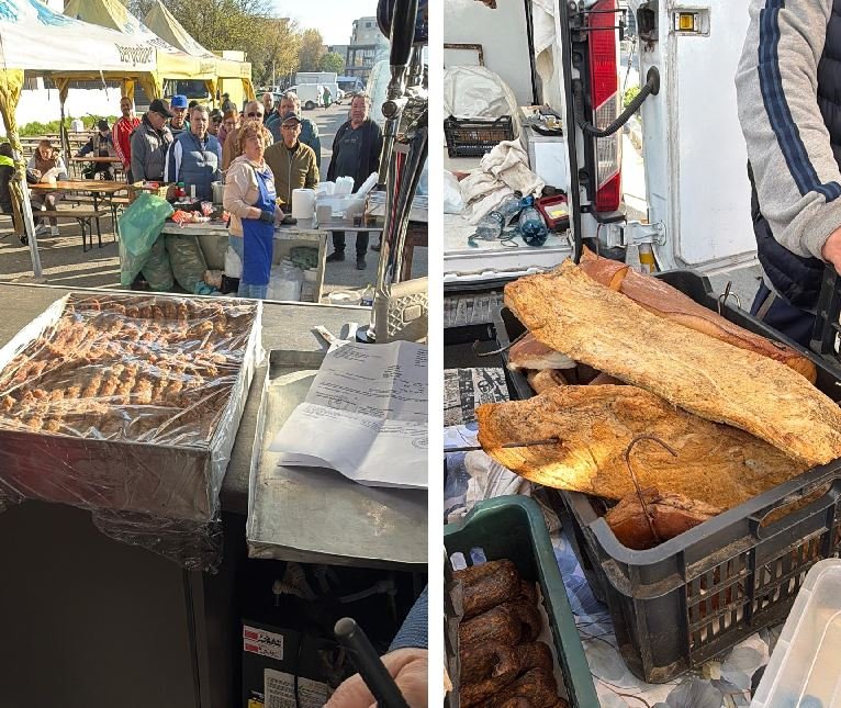 Outdoor market scene: a food stall with grilled skewers on a metal tray and customers lining up behind the counter; tents and people in the background (left). On the right, crates hold large fried flatbreads or pastries ready for sale, near a vendor's gear.
