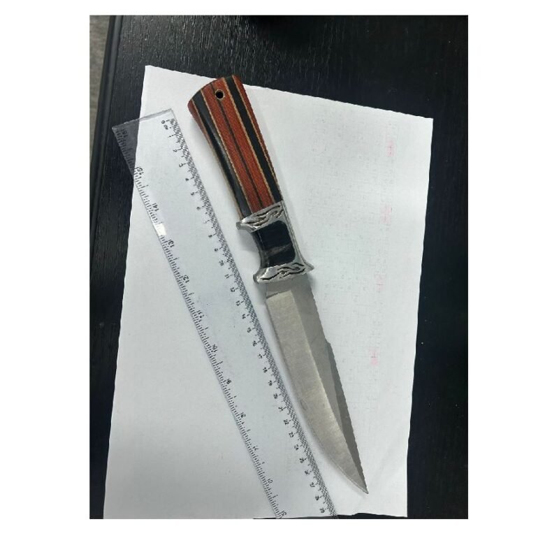 A metallic knife with a striped wooden handle resting on a sheet of white paper beside a ruler on a dark surface, viewed from above.