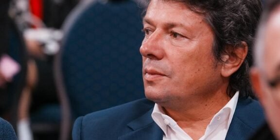 Man in a navy suit and white shirt seated at a formal event, PSD logo visible in the top-left corner.