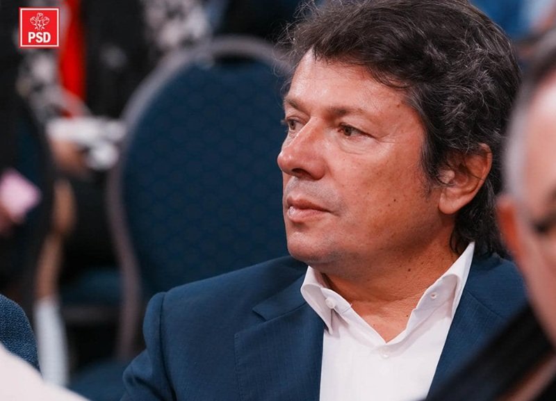 Man in a navy suit and white shirt seated at a formal event, PSD logo visible in the top-left corner.