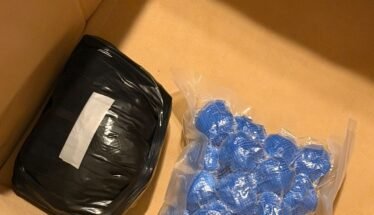 Box containing a black wrapped package and blue blister packs, with DIICOT and POLITIA ROMANA logos visible—likely seized items in a police evidence box.