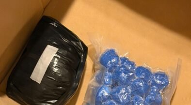 Box containing a black wrapped package and blue blister packs, with DIICOT and POLITIA ROMANA logos visible—likely seized items in a police evidence box.