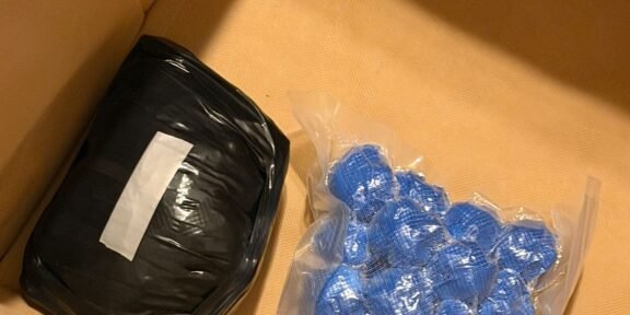 Box containing a black wrapped package and blue blister packs, with DIICOT and POLITIA ROMANA logos visible—likely seized items in a police evidence box.