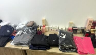 Stacks of folded jackets and clothing on a wooden table, with boxes and small items in the background.