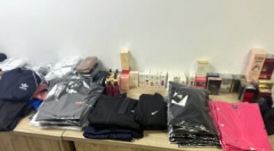 Stacks of folded jackets and clothing on a wooden table, with boxes and small items in the background.