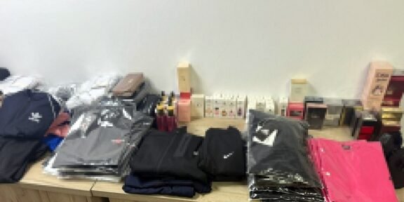Stacks of folded jackets and clothing on a wooden table, with boxes and small items in the background.