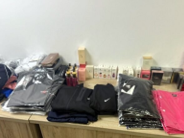 Stacks of folded jackets and clothing on a wooden table, with boxes and small items in the background.