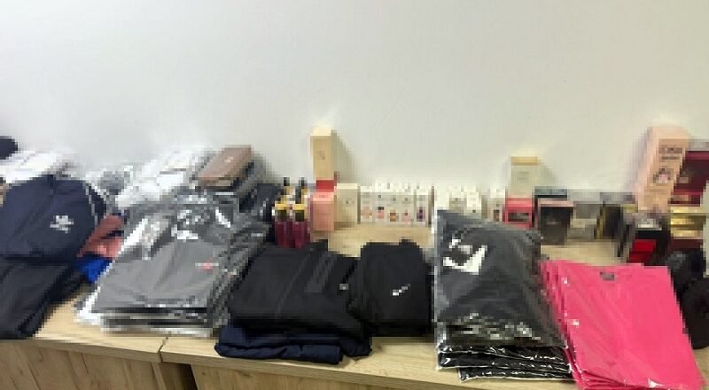 Stacks of folded jackets and clothing on a wooden table, with boxes and small items in the background.