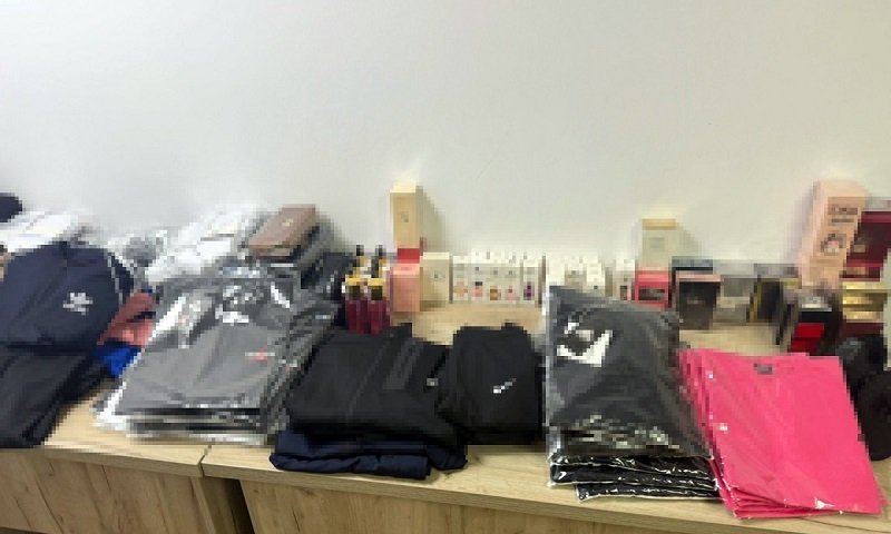 Stacks of folded jackets and clothing on a wooden table, with boxes and small items in the background.