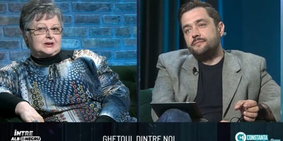 Split-screen interview on a TV talk show: an older woman in a patterned blouse on the left and a man in a gray blazer on the right, seated in a studio with blue brick and dark-blue curtain backgrounds. A bottom caption bar is visible with text.