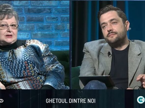 Split-screen interview on a TV talk show: an older woman in a patterned blouse on the left and a man in a gray blazer on the right, seated in a studio with blue brick and dark-blue curtain backgrounds. A bottom caption bar is visible with text.