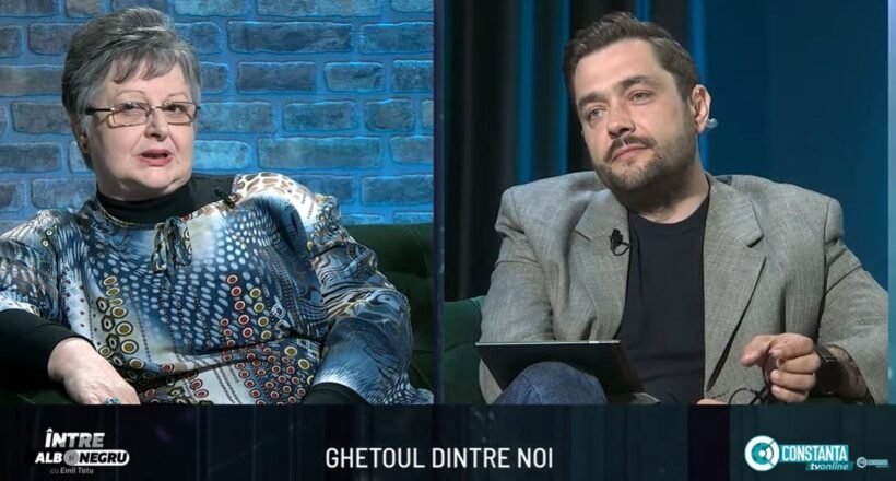 Split-screen interview on a TV talk show: an older woman in a patterned blouse on the left and a man in a gray blazer on the right, seated in a studio with blue brick and dark-blue curtain backgrounds. A bottom caption bar is visible with text.