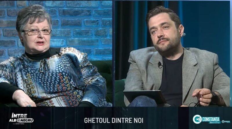 Split-screen interview on a TV talk show: an older woman in a patterned blouse on the left and a man in a gray blazer on the right, seated in a studio with blue brick and dark-blue curtain backgrounds. A bottom caption bar is visible with text.