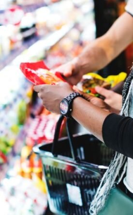 Person selecting a snack from supermarket shelves with a shopping basket nearby