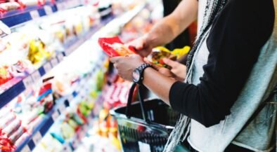 Person selecting a snack from supermarket shelves with a shopping basket nearby