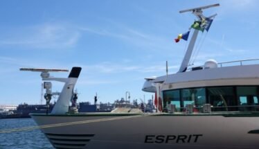 A luxury motor Yacht named Esprit moored at a marina with blue sky and flags on the mast.