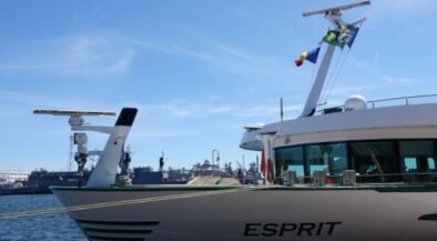 A luxury motor Yacht named Esprit moored at a marina with blue sky and flags on the mast.