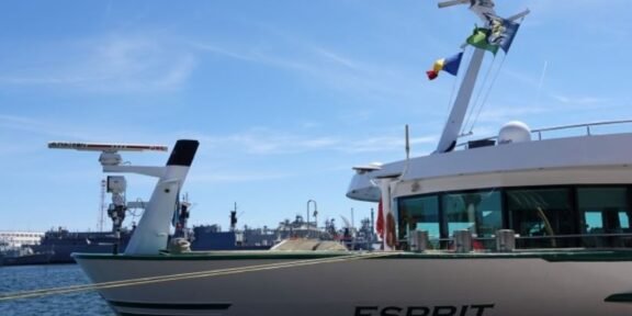 A luxury motor Yacht named Esprit moored at a marina with blue sky and flags on the mast.