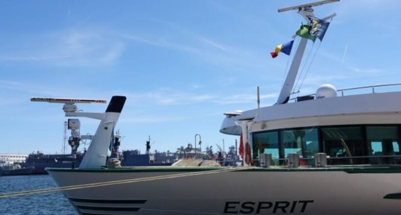A luxury motor Yacht named Esprit moored at a marina with blue sky and flags on the mast.