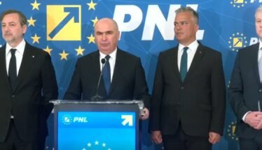 Four men in dark suits stand at a blue podium with a microphone, during a PNL press conference with EU-starry backdrop and logos behind them.