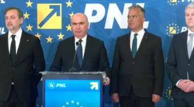 Four men in dark suits stand at a blue podium with a microphone, during a PNL press conference with EU-starry backdrop and logos behind them.