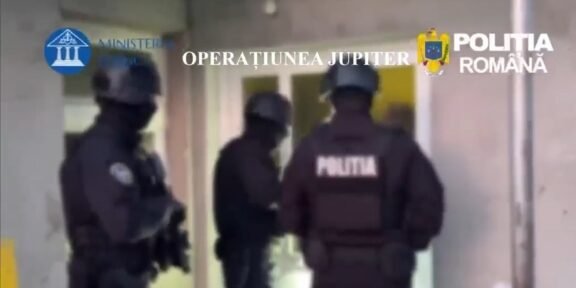 Armed Romanian police in tactical gear guard a doorway during Operation Jupiter (text overlay: OPERATIUNEA JUPITER).