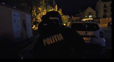 Nighttime street scene with a Romanian police officer wearing a jacket that reads POLITIA, standing near a white car on a dimly lit residential street.