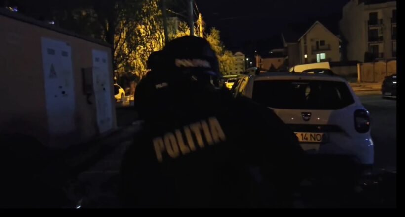 Nighttime street scene with a Romanian police officer wearing a jacket that reads POLITIA, standing near a white car on a dimly lit residential street.