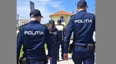 Group of police officers in dark blue uniforms labeled POLITIA walking along a sidewalk past a yellow house.