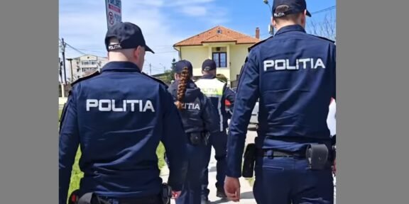 Group of police officers in dark blue uniforms labeled POLITIA walking along a sidewalk past a yellow house.