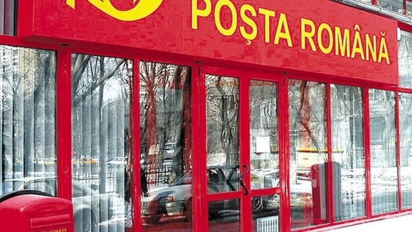 Front of a Poșta Română post office with a red facade, glass doors, and a red mailbox outside in the snow.