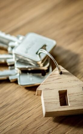Keys on a keyring with a small wooden house tag, placed on a wood surface, symbolizing home ownership or real estate access.