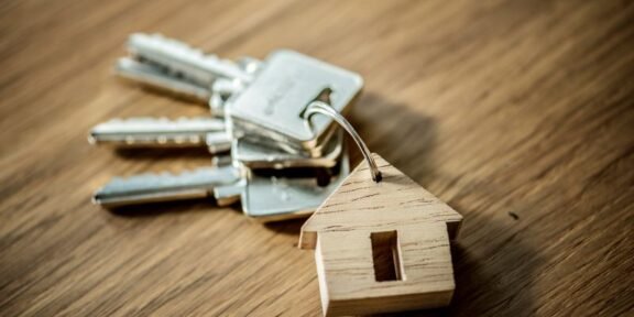 Keys on a keyring with a small wooden house tag, placed on a wood surface, symbolizing home ownership or real estate access.