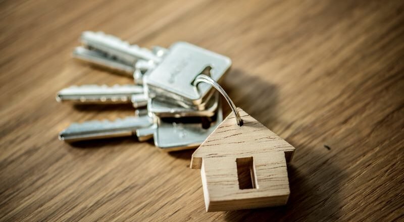 Keys on a keyring with a small wooden house tag, placed on a wood surface, symbolizing home ownership or real estate access.
