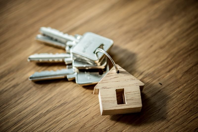 Keys on a keyring with a small wooden house tag, placed on a wood surface, symbolizing home ownership or real estate access.