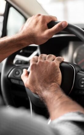 Hands on a car steering wheel with both hands, driver in control of the vehicle.