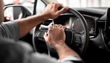 Hands on a car steering wheel with both hands, driver in control of the vehicle.