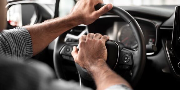 Hands on a car steering wheel with both hands, driver in control of the vehicle.