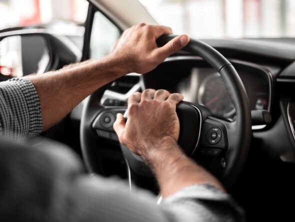 Hands on a car steering wheel with both hands, driver in control of the vehicle.