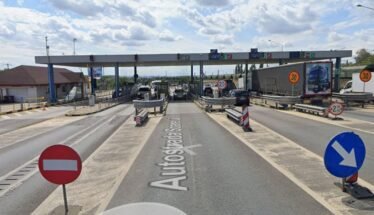 Toll plaza on a highway with multiple lanes, barriers, and cars waiting to pass under an overhead canopy.