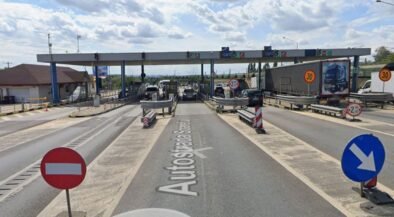 Toll plaza on a highway with multiple lanes, barriers, and cars waiting to pass under an overhead canopy.