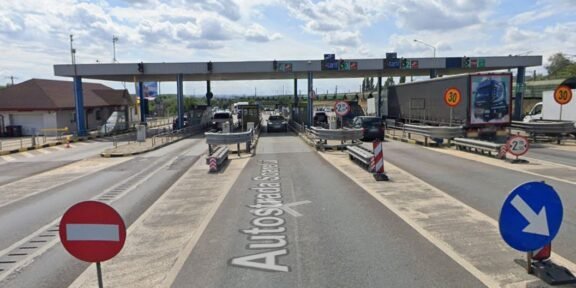 Toll plaza on a highway with multiple lanes, barriers, and cars waiting to pass under an overhead canopy.