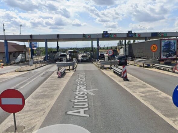 Toll plaza on a highway with multiple lanes, barriers, and cars waiting to pass under an overhead canopy.