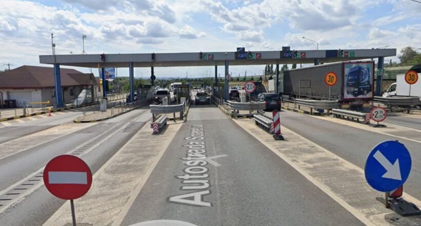 Toll plaza on a highway with multiple lanes, barriers, and cars waiting to pass under an overhead canopy.