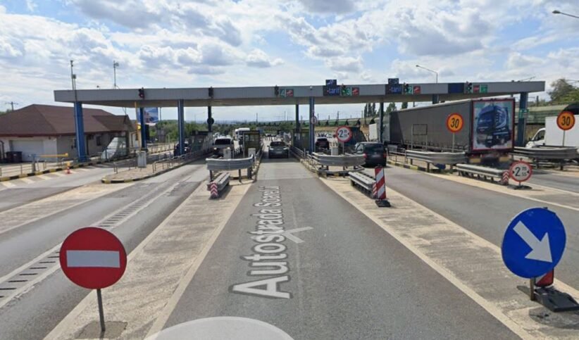 Toll plaza on a highway with multiple lanes, barriers, and cars waiting to pass under an overhead canopy.