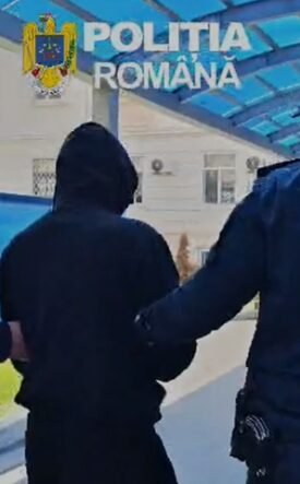 Two Romanian police officers escort a hooded person outdoors under a blue canopy labeled Politia Romana.