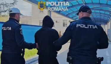 Two Romanian police officers escort a hooded person outdoors under a blue canopy labeled Politia Romana.